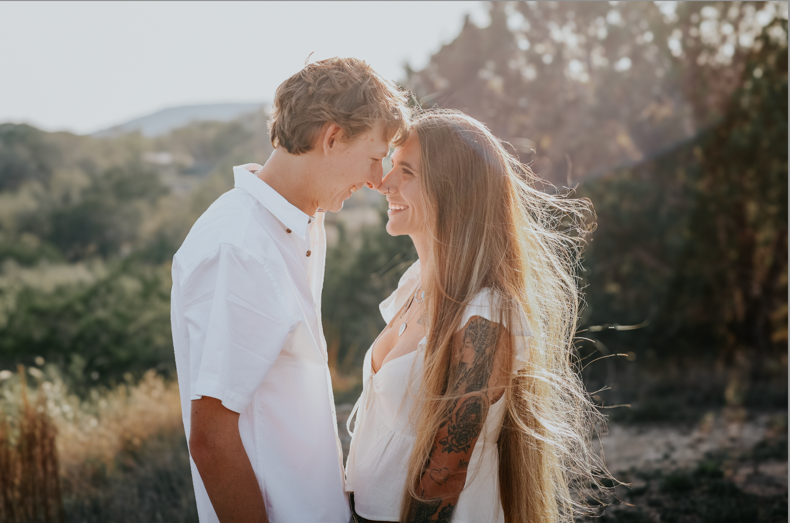 Couple embracing at golden hour with windswept hair, mountains in the background