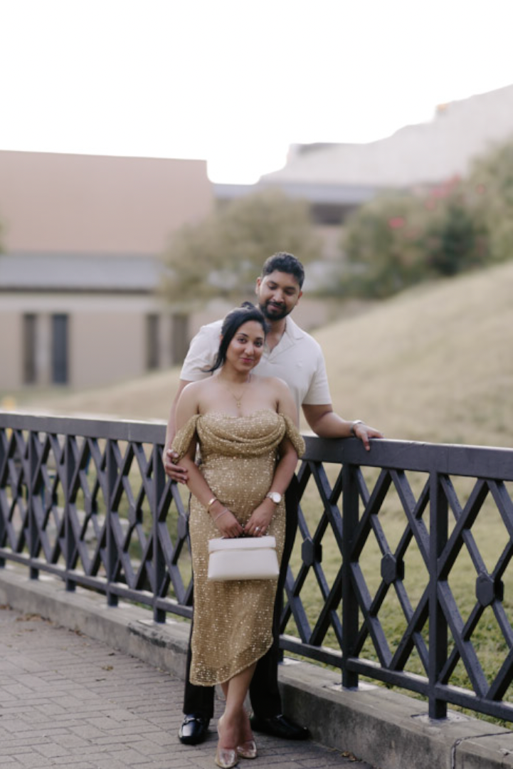 Couple standing together at a bridge railing, woman in a gold dress