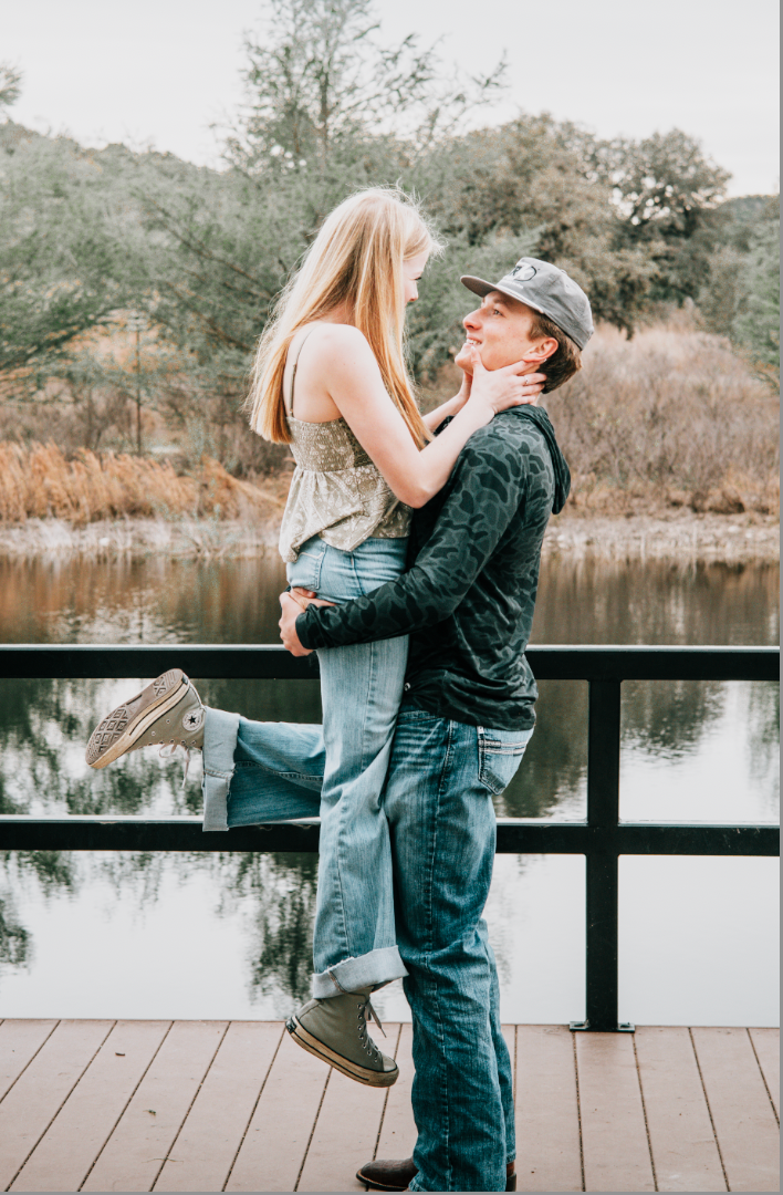 Man joyfully lifting woman off the ground beside a lake