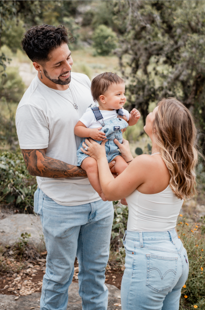 Parents holding their baby up between them, laughing outdoors