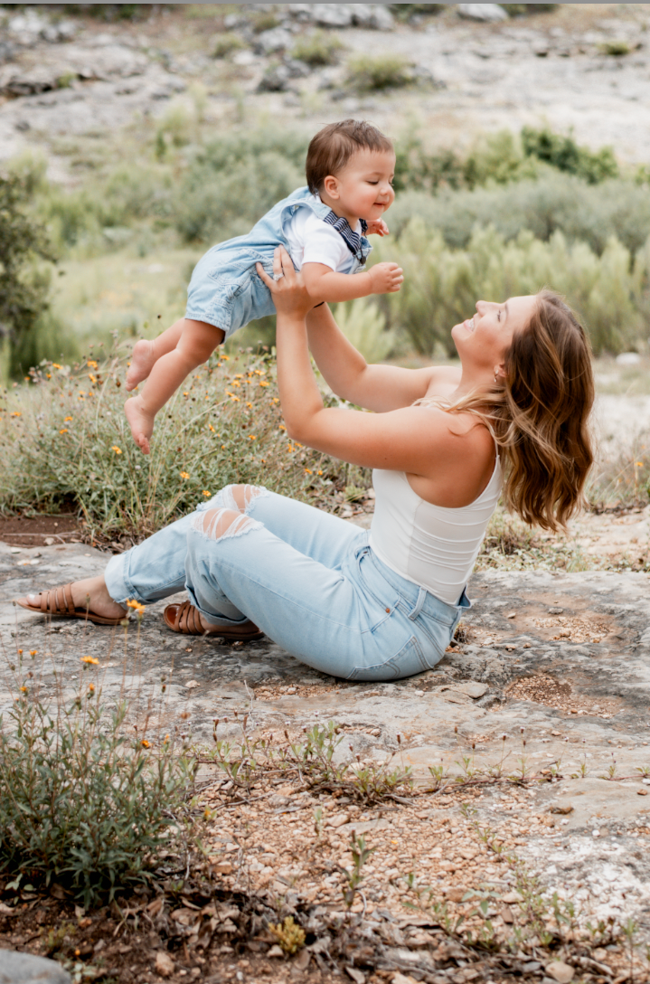 Mother lifting her laughing baby into the air on a rocky hillside