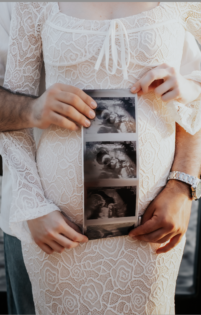 Expecting parents holding a sonogram photo strip, wider framing