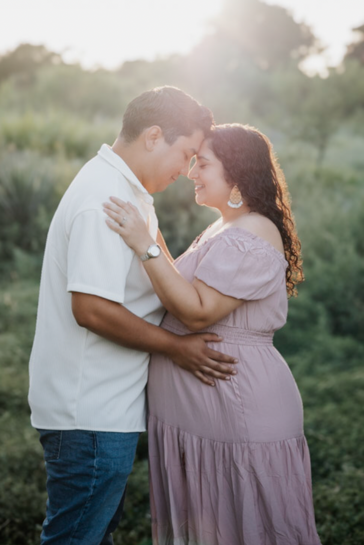 Couple embracing forehead to forehead at golden hour, pregnant belly between them