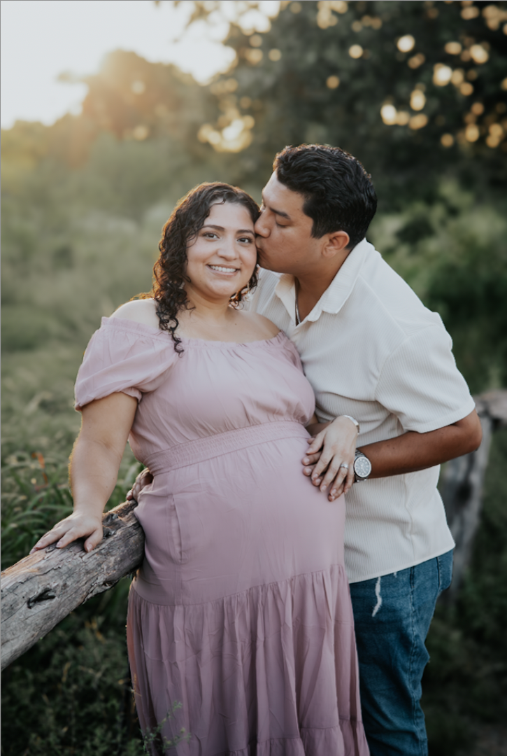 Man kissing his partner's cheek, hand resting on her pregnant belly at golden hour