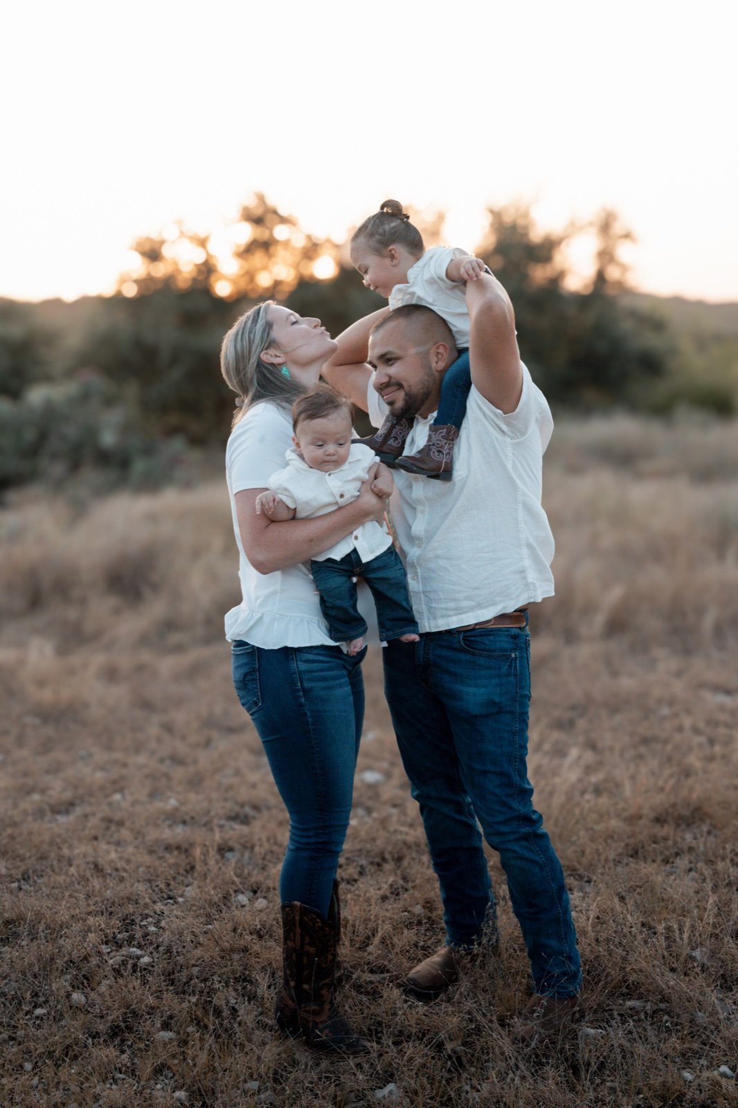 Parents laughing with their two young children in a golden-hour field