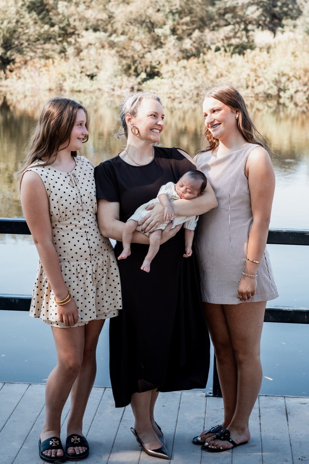 Mother and her two older daughters gathered close around the new baby by the water