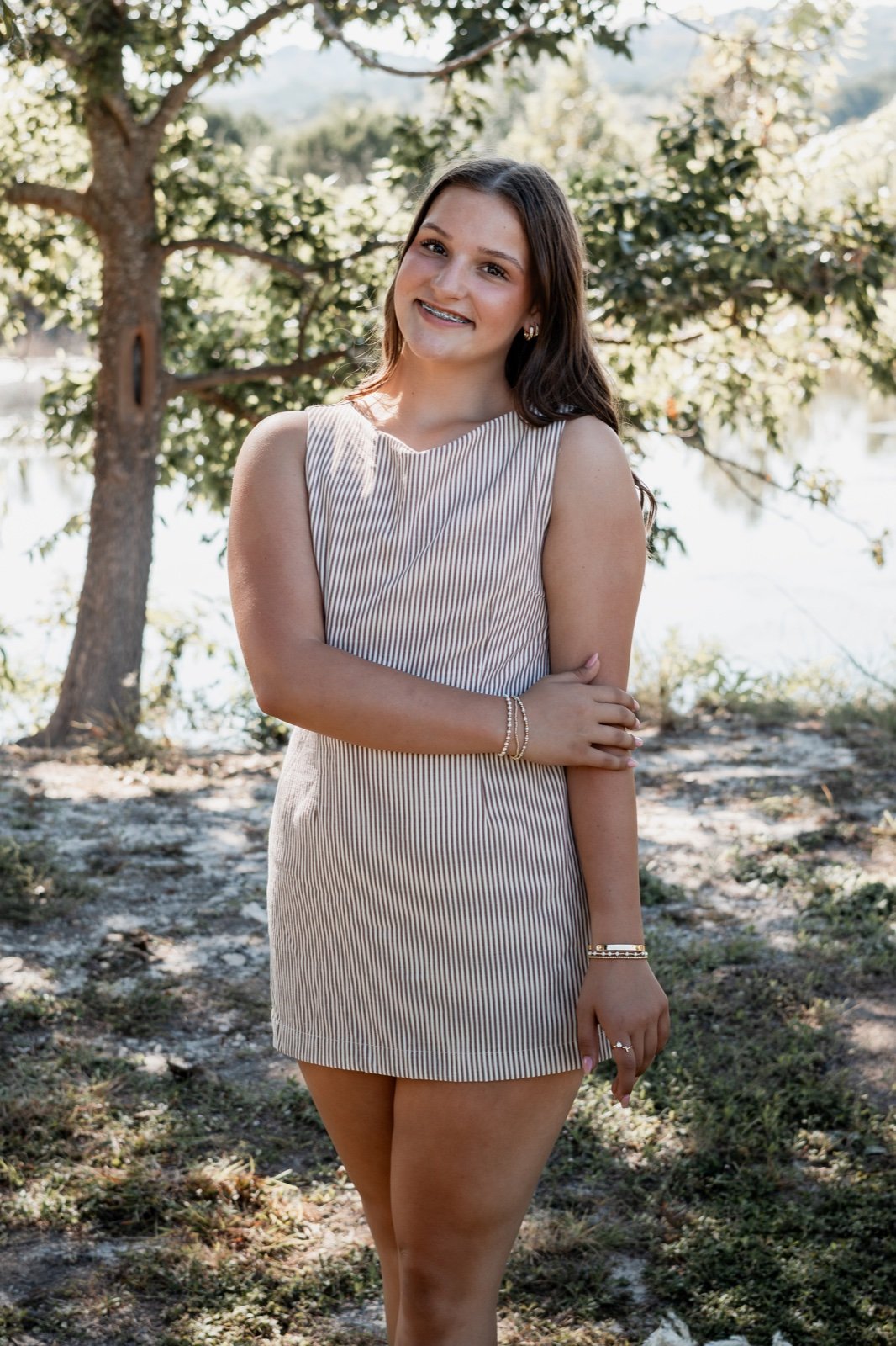 Teenage girl smiling under a tree beside the water